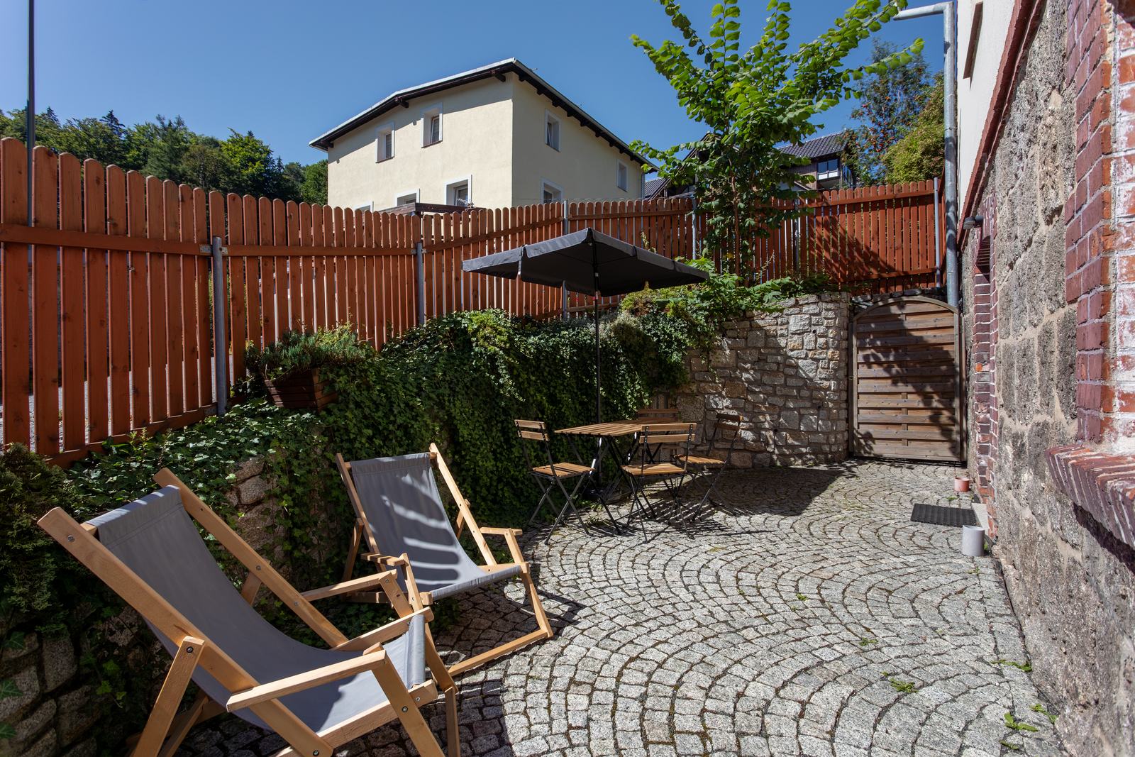 Prywatne patio z leżakami, stolikiem i parasolem przy kamiennym murze