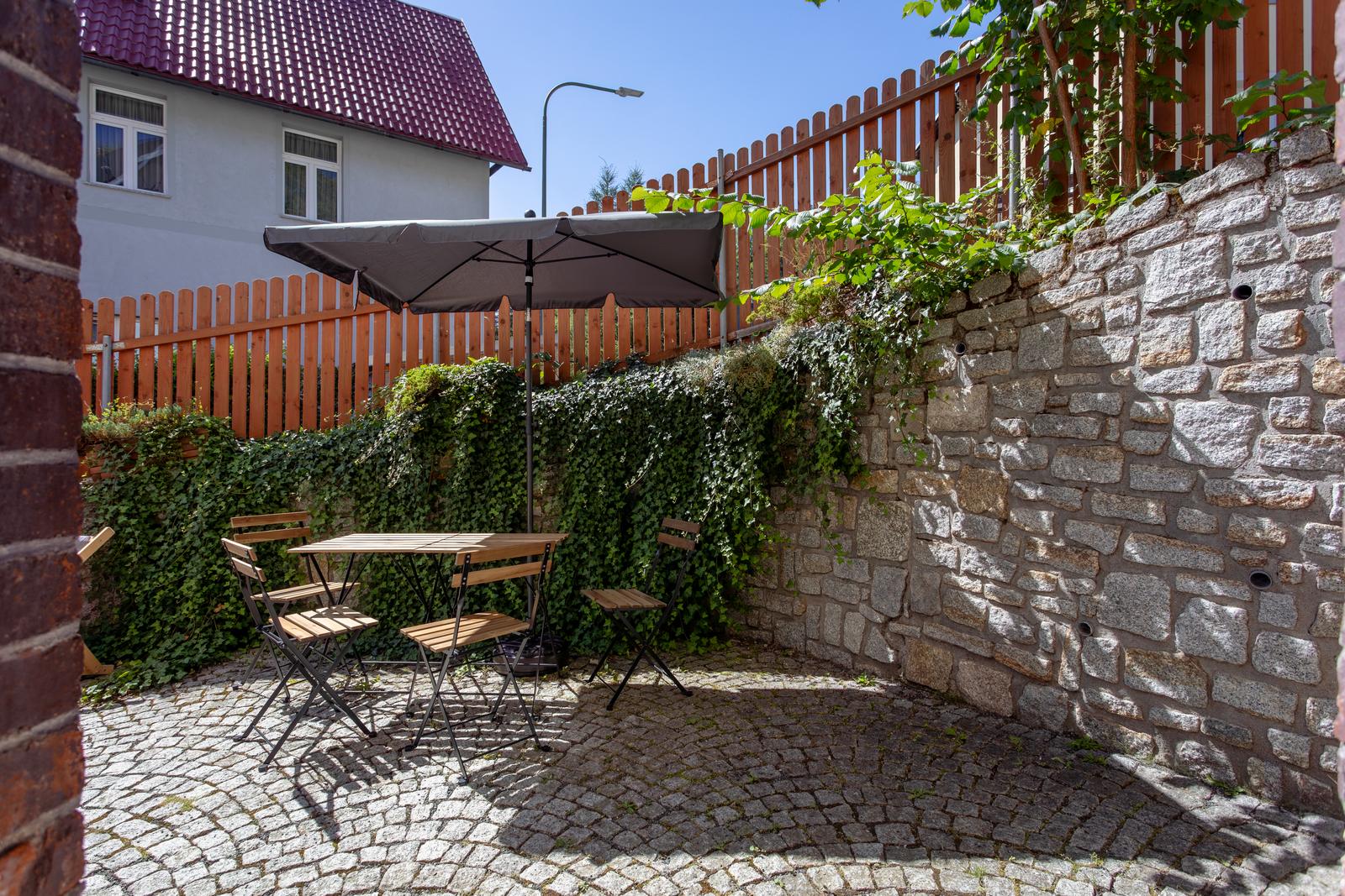 Stolik z krzesłami pod parasolem na patio z kamiennym murem i bluszczem
